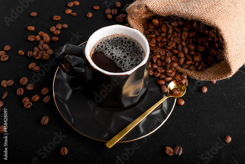 Una taza de café negro con una cucharita dorada al costado, y granos de café esparcido   photo