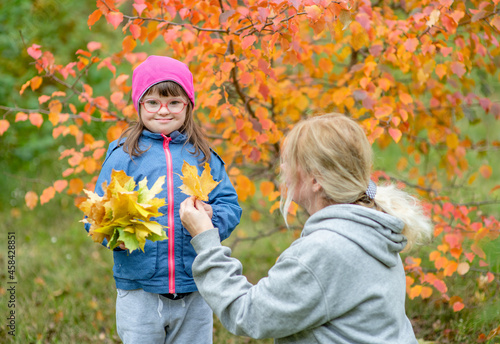 Mother and little girl with special needs have a fun in autumn park