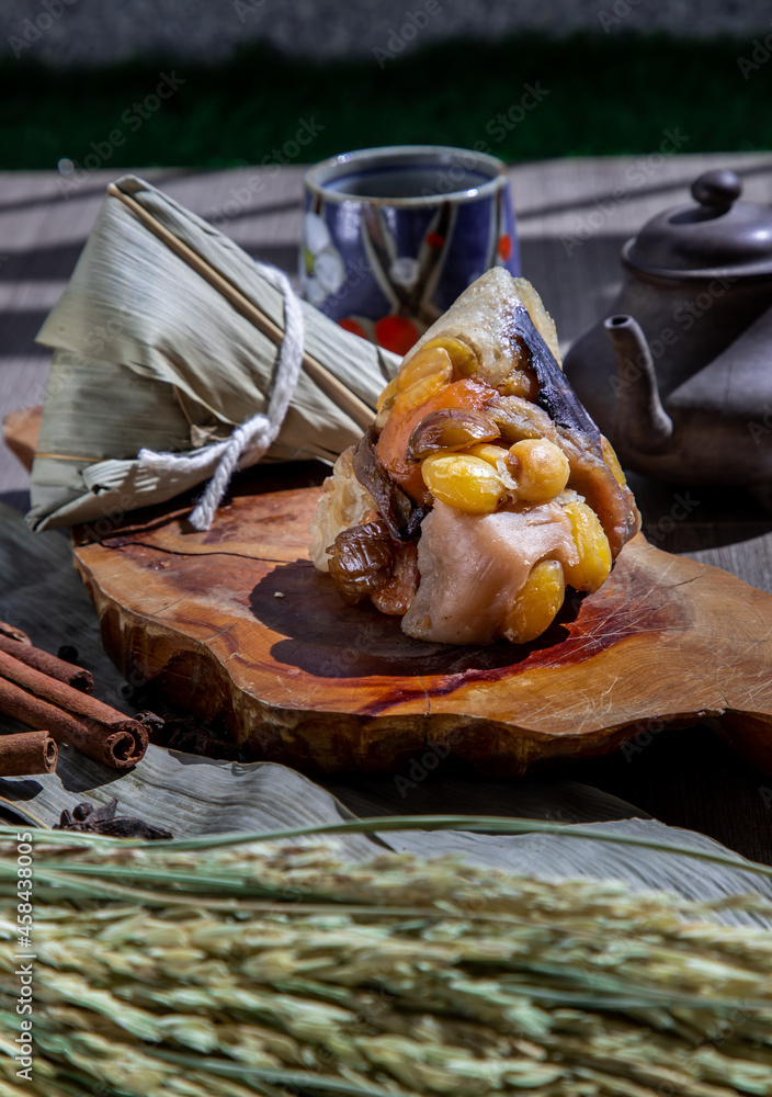 Chinese rice dumpling (Zongzi) shaped pyramidal wrapped by leaves ingredients on wooden plate Served with chinese tea and chopsticks. Famous asian tasty handmade food in dragon boat (duan wu) festival