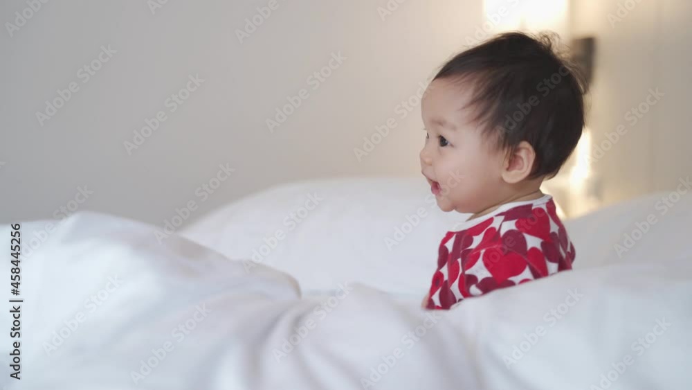 portrait of asian baby infant 8 months old playing on bed at home. happy innocence baby kid smile happily. sucking hand age baby portrait crawling copy space provided. smiling baby laugh in bedroom.
