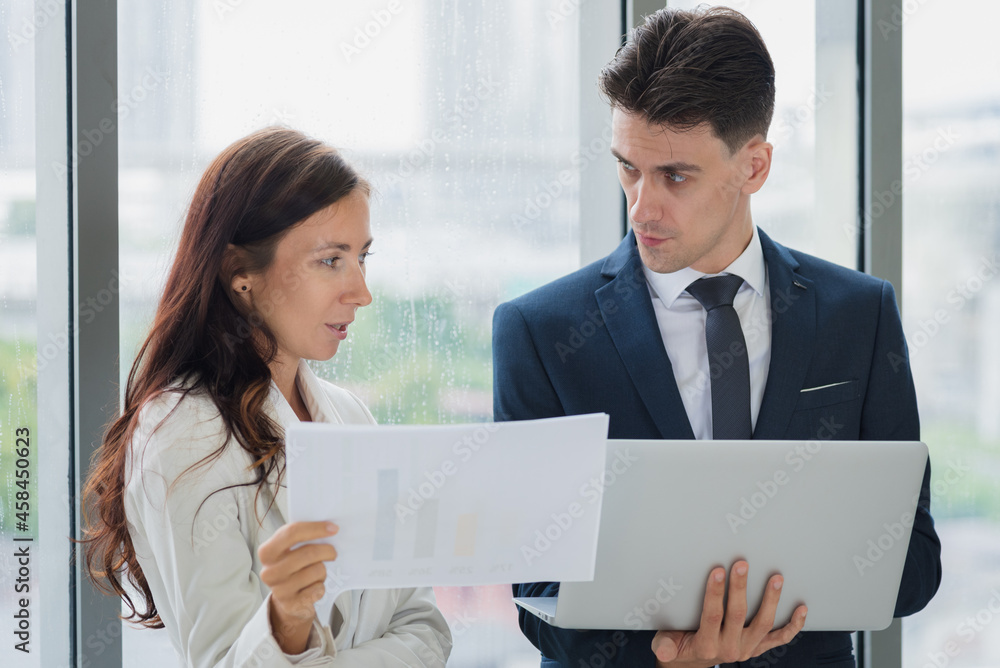 Portrait of adult business man and woman in formal work suit outfit standing and discuss about company investment in modern office room Portrait of adult business man and woman in formal work suit outfit standing and discuss about company investment in modern office room