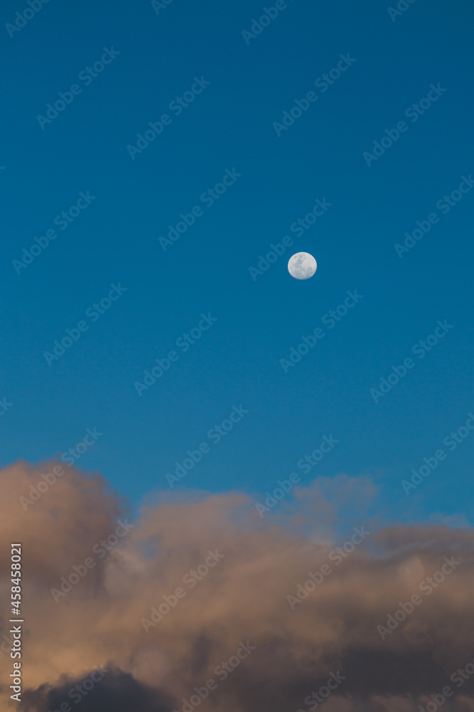 full moon with pink fluffy clouds underneath it in the blue sky at dusk full moon with pink fluffy clouds underneath it in the blue sky at dusk
