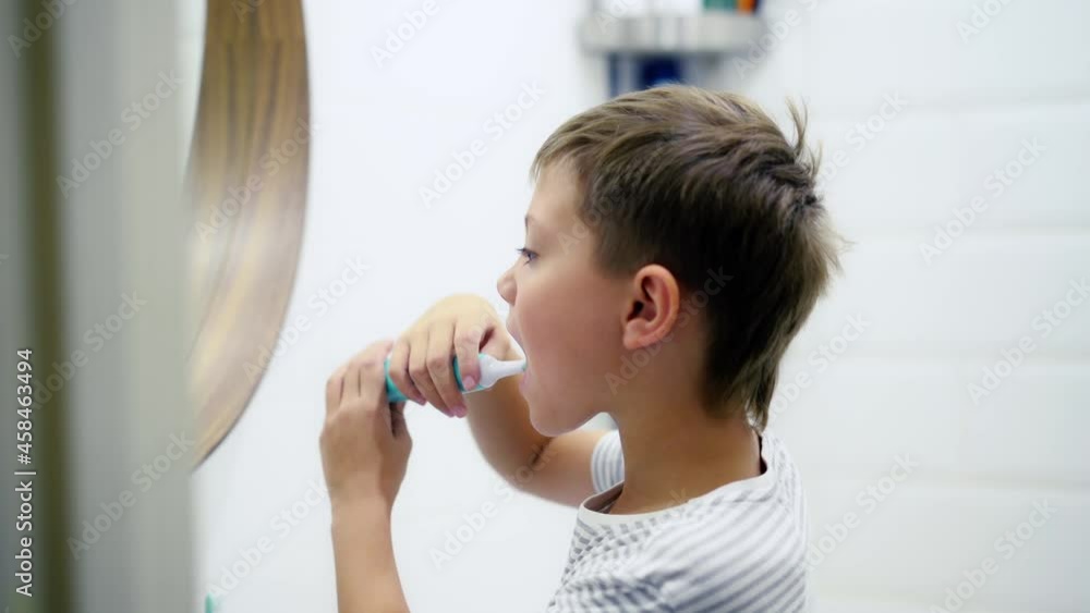 cute caucasian boy brushing his teeth with electric brush looking in the mirror cute caucasian boy brushing his teeth with electric brush looking in the mirror