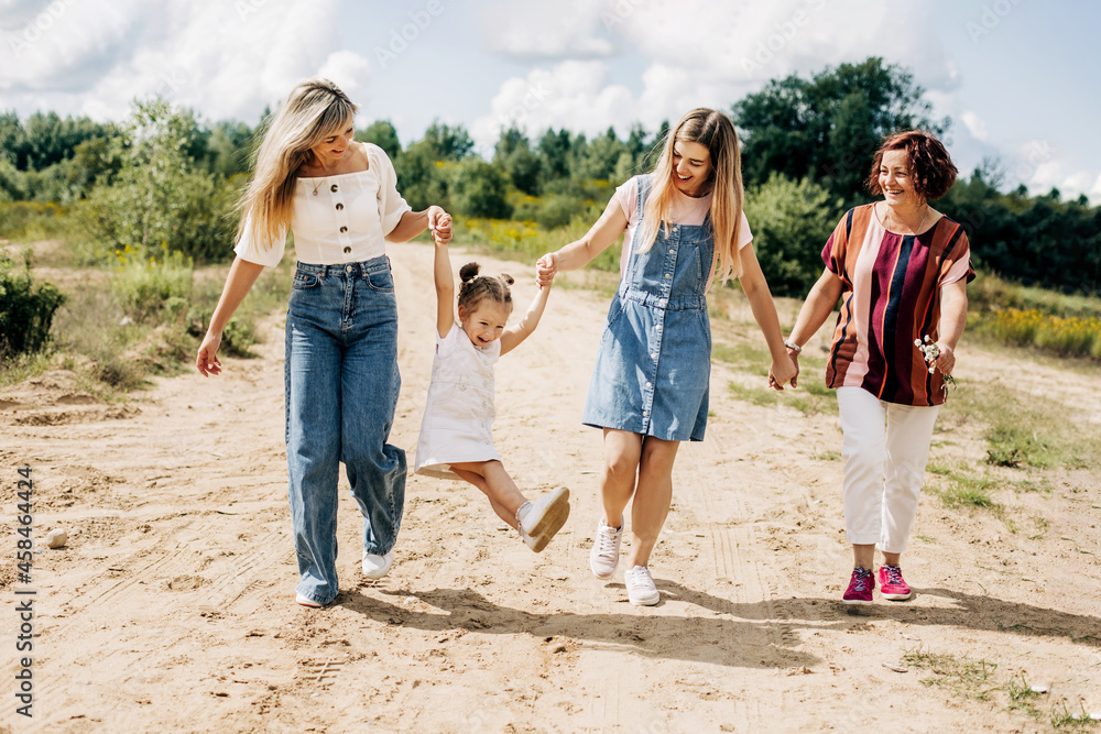 Several generations of women of the same family are walking along a dirt road outside the city, enjoying the time spent together Several generations of women of the same family are walking along a dirt road outside the city, enjoying the time spent together