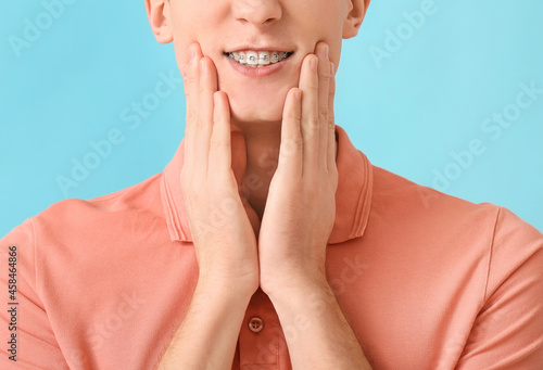 Handsome man with dental braces on color background, closeup photo