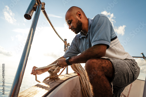 Canvastavla Young african american sailor tying ropes on sailboat in the sea on sunset