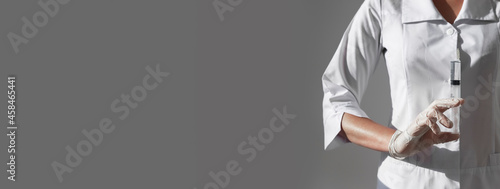 Syringe with sharp needle in doctors or nurse hands on gray banner with copy space for text.