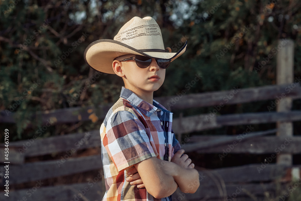 Portrait of a little boy in a cowboy hat and a plaid shirt in the countryside .