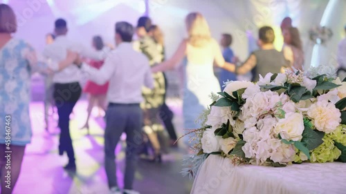 Guests dancing moldavian national dance - Hora at a wedding. Bouquet on the foreground. Stage lights