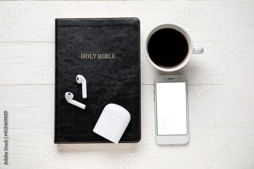 Holy Bible, earphones, mobile phone and cup of coffee on light wooden background