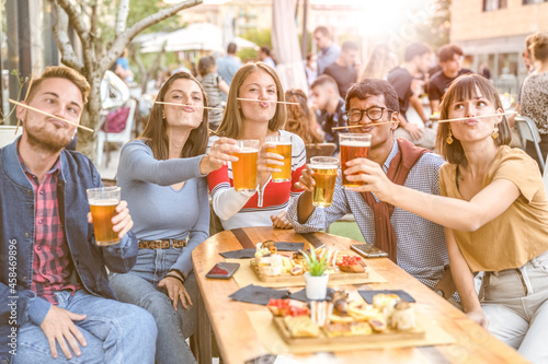 young university people having fun  group of friends eating food and drinking beer at restaurant  millennials outdoor leisure  warm filter and backlight sunset