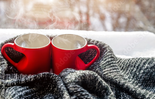 two heart shaped mugs with tea on the background of a window in winter
