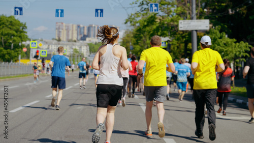Photography Contestants of city marathon running on asphalt road, focus on woman with ponytail, buildings on blurred background