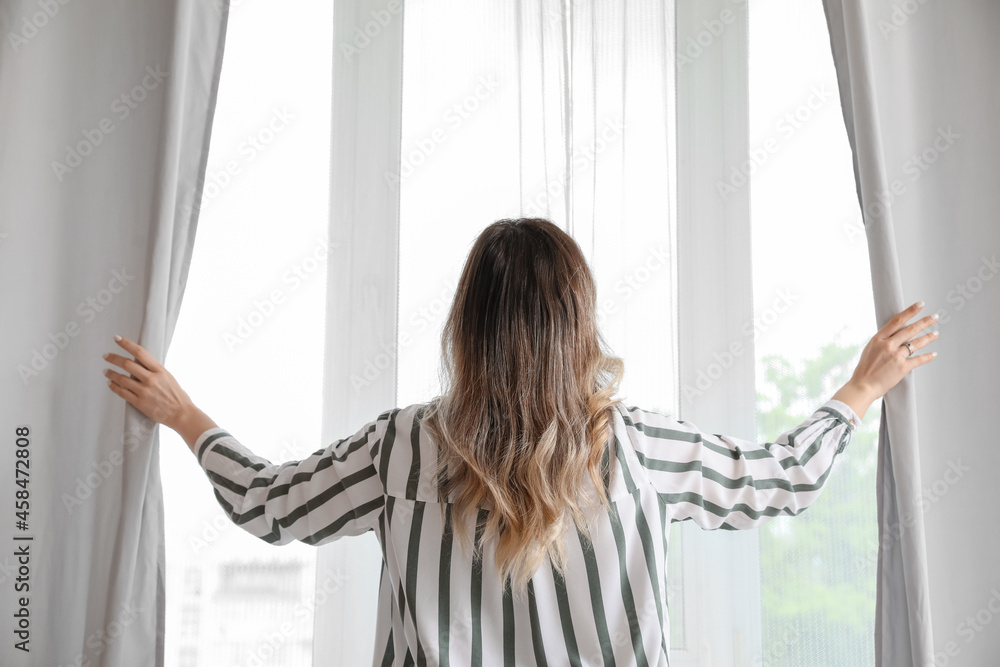 Fototapeta premium Woman opening light curtains in morning at home