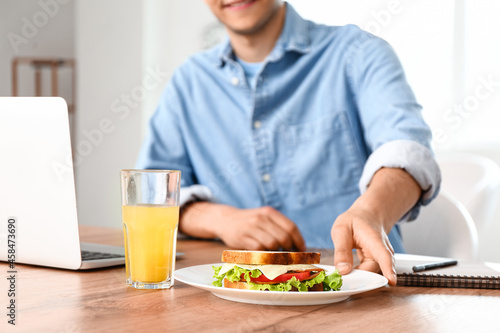 Young man with tasty sandwich in office