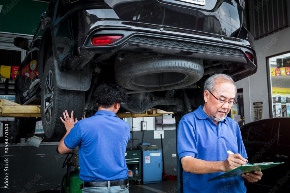 Senior foreman checking list of vehicle repair service while two mechanic checking wheel, inspecting under car body of customer car at automobile garage service, vehicle repair service shop concept Senior foreman checking list of vehicle repair service while two mechanic checking wheel, inspecting under car body of customer car at automobile garage service, vehicle repair service shop concept
