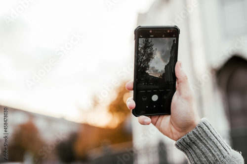male hands in a gray sweater holding a black phone on the street in the city in nature against the background of the river and bridge