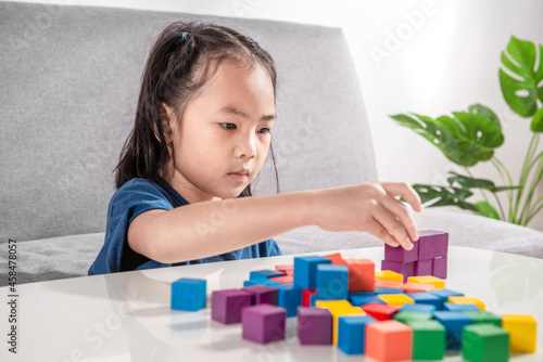 Asian girl plays with small wooden colorful toy blocks at home or kindergarten. A Girl serious playing with construction blocks for toddler kids. Education Development Construction creative toys Idea