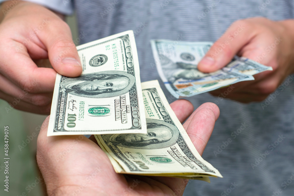 one person passes another a bundle of hundred dollar bills counting them one person passes another a bundle of hundred dollar bills counting them