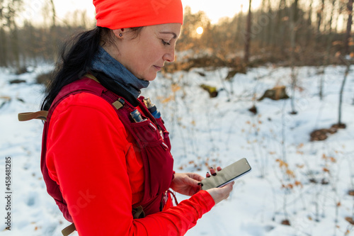 Woman Checking Mobile While Running in Woods. Female Runner Holding Cellphone in Hands On Cold Winter Day.