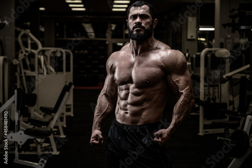 powerful young strong bearded male with athletic body in gym at night