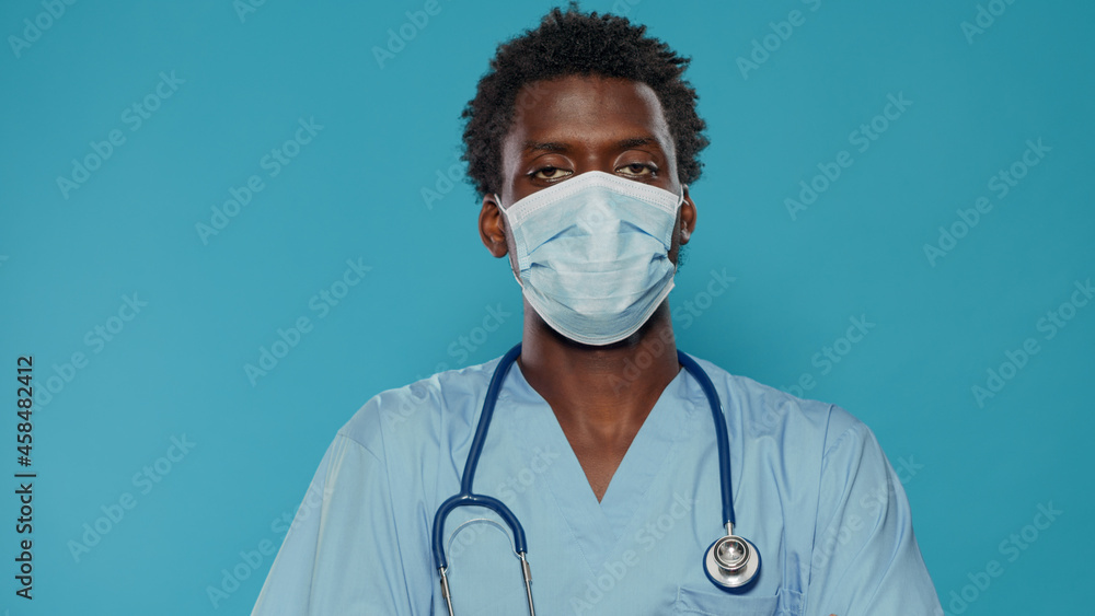 Close up of medical assistant with face mask looking at camera in studio. Portrait of man working as nurse, wearing blue uniform and stethoscope while having protection against covid 19 Close up of medical assistant with face mask looking at camera in studio. Portrait of man working as nurse, wearing blue uniform and stethoscope while having protection against covid 19