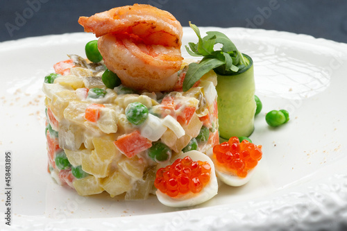 Traditional Russian salad with egg, peas, potatoes and mayonnaise on a plate.