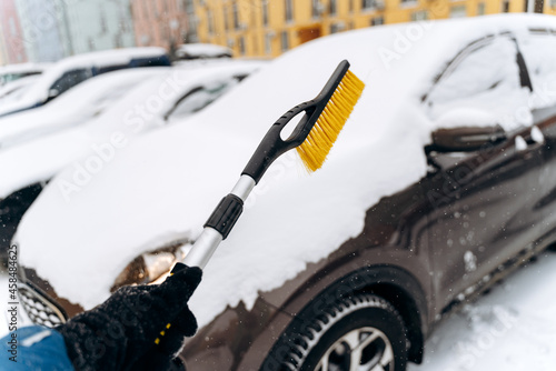 Cropped view of the unrecognizable person using special brush for cleaning car from the snow. Parked car covered with snow after snowfall in winter