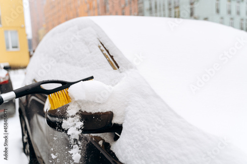 Close up view of the unrecognizable person cleaning car from the snow with the special brush. Device for cleaning snow from the car concept. Stock photo