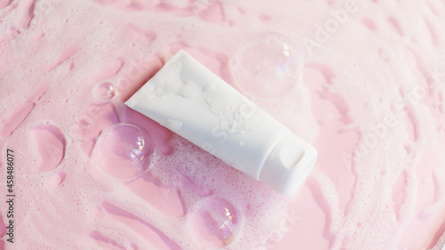 white cosmetic tube for shower gel, face or body cleancer on a pink background with soap foam and bubbles. The concept of a cleansing cosmetic product