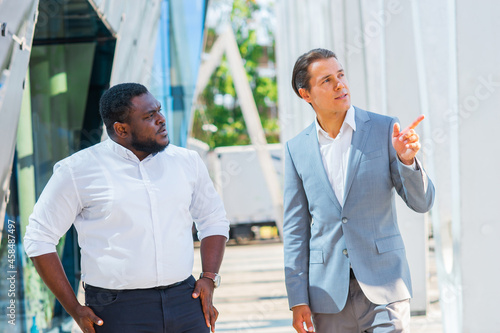 African-American businessman and his colleague in front of modern office building. Financial investors are talking outdoor. Banking and business concept.