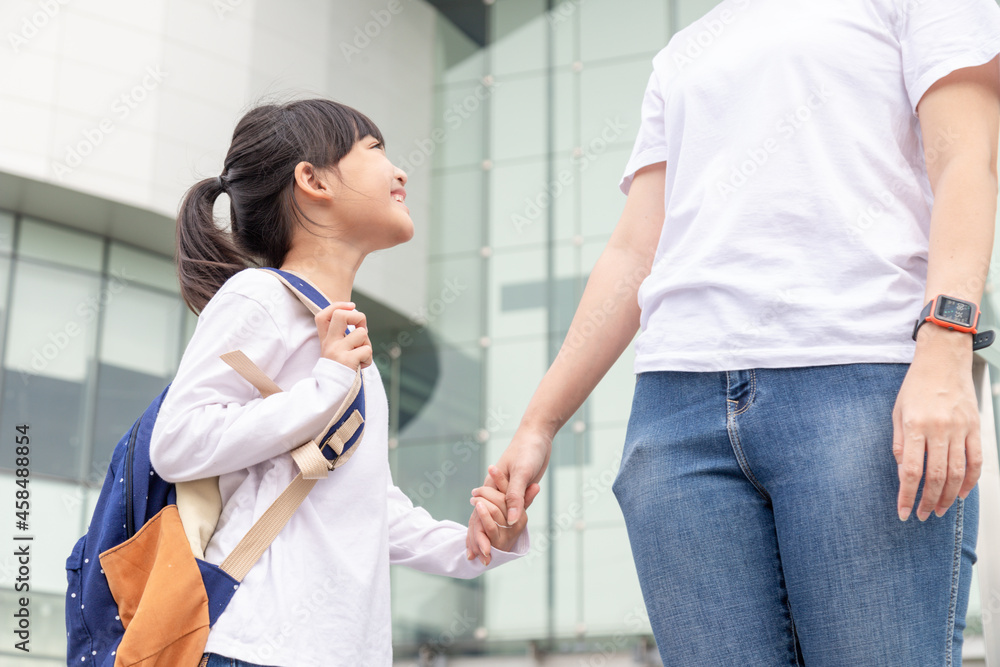 Fototapeta premium Back to school. Asian mother and daughter pupil girl with backpack holding hand and going to school together. Beginning of lessons. First day