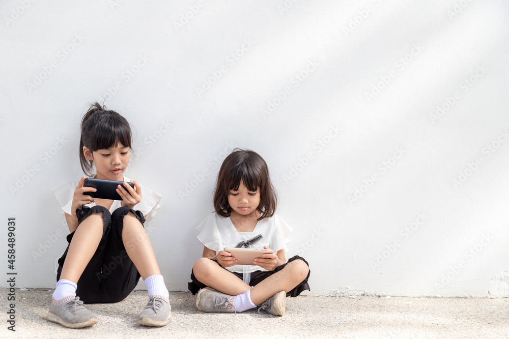 Concept kids and gadgets. Two little girls siblings sisters look at the phone and smile. They hold a smartphone watch videos, learn, play games, speak online. Internet for children. Parental control Concept kids and gadgets. Two little girls siblings sisters look at the phone and smile. They hold a smartphone watch videos, learn, play games, speak online. Internet for children. Parental control