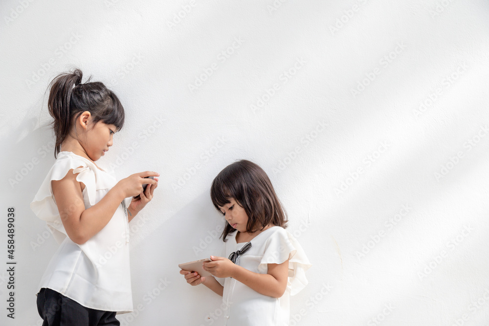Sibling girls watching their smartphones on white background. Social concept about new technology people addiction Sibling girls watching their smartphones on white background. Social concept about new technology people addiction