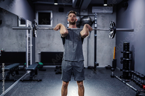 Cross-fit exercises. A shot of a handsome man lifting a barbell with weights and pumping up his muscles in a modern sports center. A motivated person in good physical shape does the training