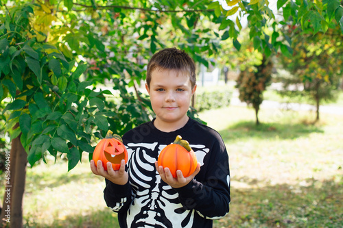 Smiling boy in black costume of skeleton holding two small decorative halloween pumpkins.
