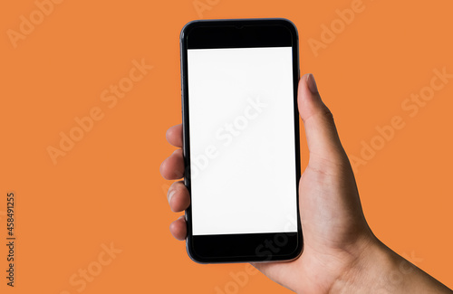 Female holding a black smartphone with a touch screen in orange background.