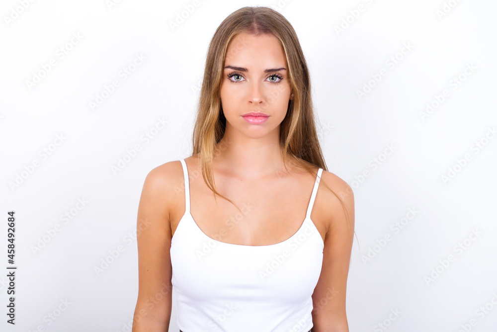 Joyful beautiful blonde girl wearing sexy t-shirt on white background looking to the camera, thinking about something. Both arms down, neutral facial expression. Joyful beautiful blonde girl wearing sexy t-shirt on white background looking to the camera, thinking about something. Both arms down, neutral facial expression.
