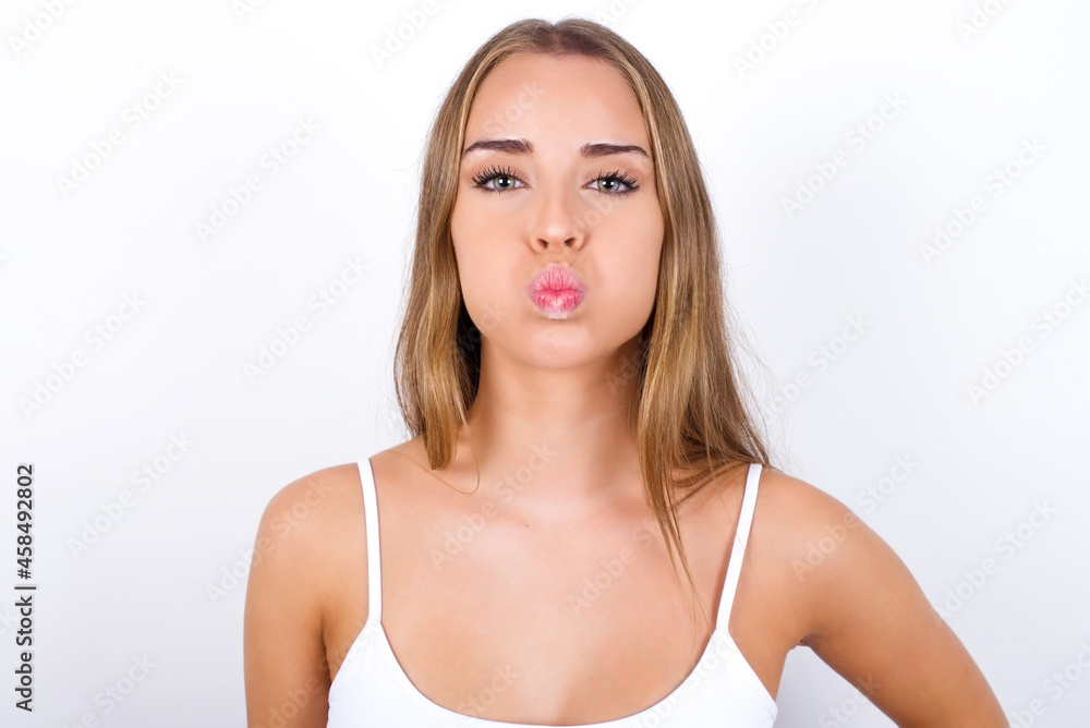 beautiful blonde girl wearing sexy t-shirt on white background puffing cheeks with funny face. Mouth inflated with air, crazy expression. beautiful blonde girl wearing sexy t-shirt on white background puffing cheeks with funny face. Mouth inflated with air, crazy expression.