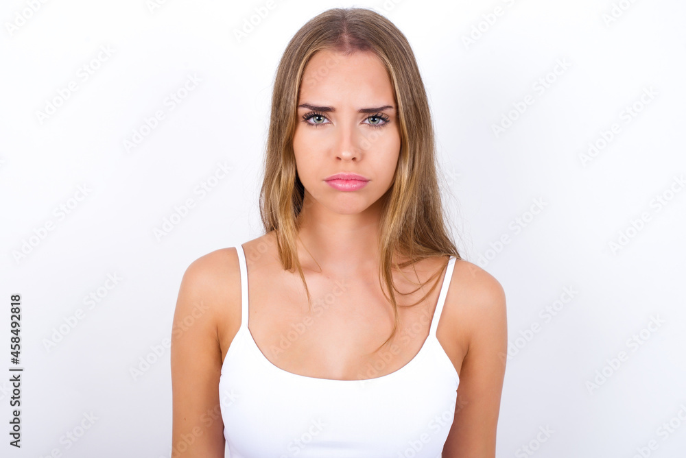 beautiful blonde girl wearing sexy t-shirt on white background frowning his eyebrows being displeased with something. beautiful blonde girl wearing sexy t-shirt on white background frowning his eyebrows being displeased with something.