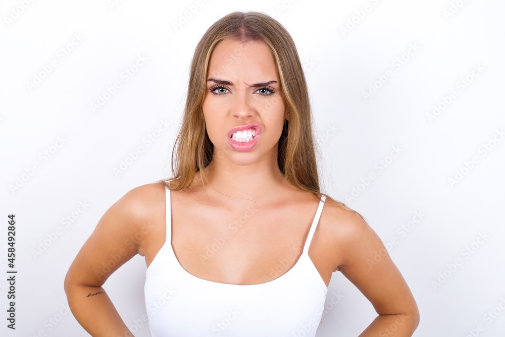 Mad crazy beautiful blonde girl wearing sexy t-shirt on white background clenches teeth angrily, being annoyed with coming noise. Negative feeling concept. Mad crazy beautiful blonde girl wearing sexy t-shirt on white background clenches teeth angrily, being annoyed with coming noise. Negative feeling concept.