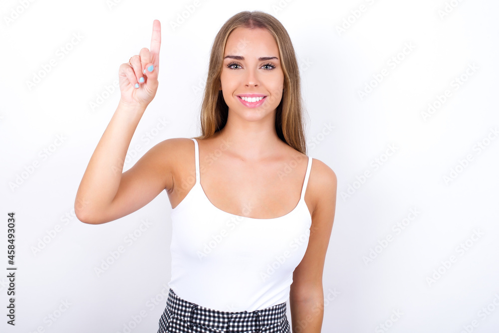 beautiful blonde girl wearing sexy t-shirt on white background showing and pointing up with fingers number one while smiling confident and happy. beautiful blonde girl wearing sexy t-shirt on white background showing and pointing up with fingers number one while smiling confident and happy.
