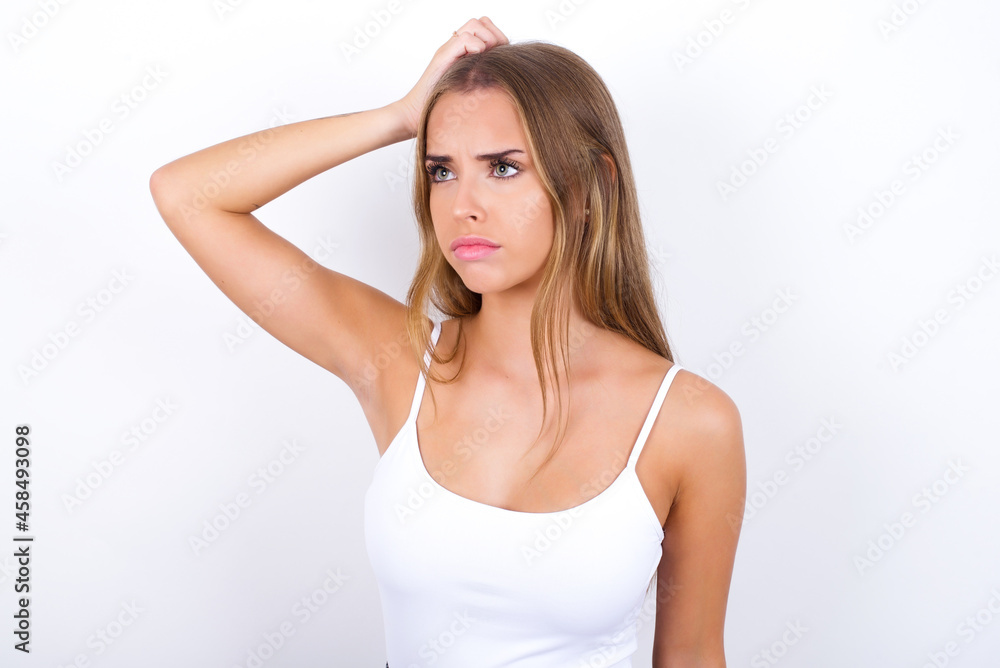 beautiful blonde girl wearing sexy t-shirt on white background saying: Oops, what did I do? Holding hand on head with frightened and regret expression. beautiful blonde girl wearing sexy t-shirt on white background saying: Oops, what did I do? Holding hand on head with frightened and regret expression.