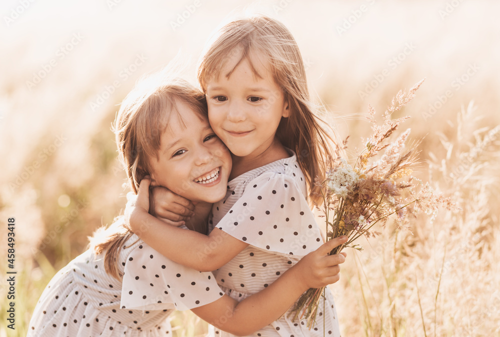 Two little happy identical twin girls playing together in nature in summer. Girls friendship and youth concept. Active children's lifestyle. - obrazy, fototapety, plakaty 