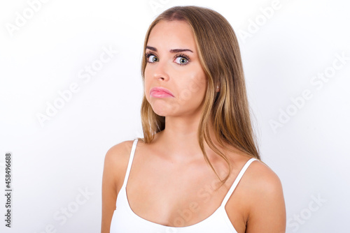 beautiful blonde girl wearing sexy t-shirt on white background with snobbish expression curving lips and raising eyebrows, looking with doubtful and skeptical expression, suspect and doubt.