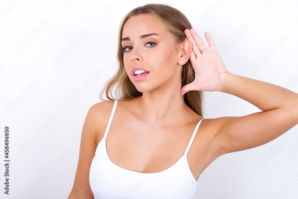 Oh my God! Funny astonished beautiful blonde girl wearing sexy t-shirt on white background opening mouth widely looking aside, with hand near ear trying to listen to gossips. Oh my God! Funny astonished beautiful blonde girl wearing sexy t-shirt on white background opening mouth widely looking aside, with hand near ear trying to listen to gossips.