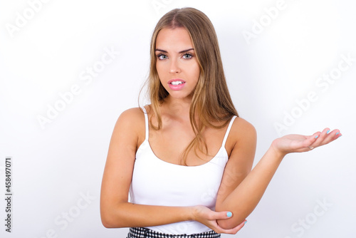 Studio shot of frustrated  beautiful blonde girl wearing sexy t-shirt on white background gesturing with raised palm, frowning, being displeased and confused with dumb question. © Jihan