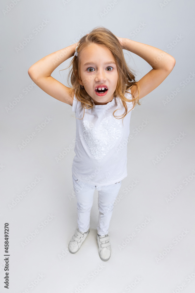 High angle view of beautiful little girl with long hair in modern stylish outfit posing isolated on white studio background. Happy childhood concept. High angle view of beautiful little girl with long hair in modern stylish outfit posing isolated on white studio background. Happy childhood concept.
