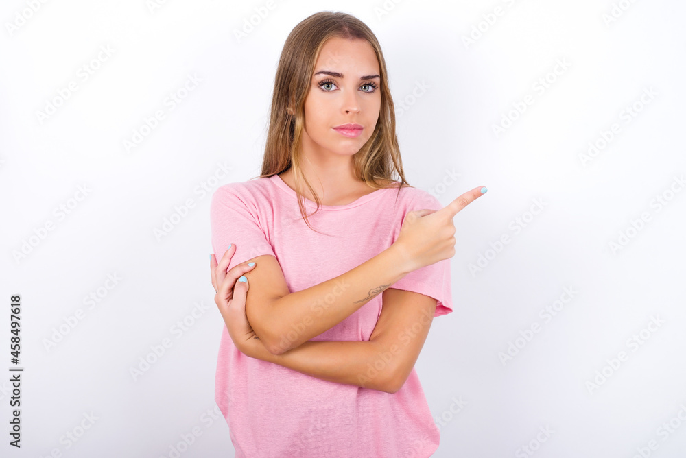 beautiful blonde girl wearing pink t-shirt on white background smiling broadly at camera, pointing fingers away, showing something interesting and exciting. beautiful blonde girl wearing pink t-shirt on white background smiling broadly at camera, pointing fingers away, showing something interesting and exciting.