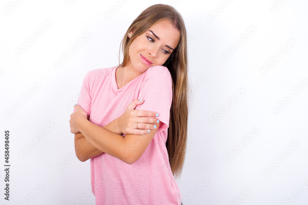 beautiful blonde girl wearing pink t-shirt on white background Hugging oneself happy and positive, smiling confident. Self love and self care. beautiful blonde girl wearing pink t-shirt on white background Hugging oneself happy and positive, smiling confident. Self love and self care.